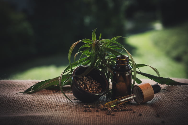 Boccetta con olio di CBD utilizzato a scopo terapeutico, con accanto semi di cannabis e foglie di marijuana