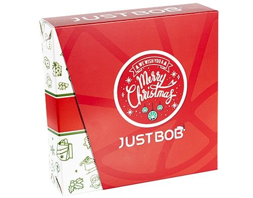 Scatola Justbob XMAS KIT in rosso e bianco con messaggio 'Ti auguriamo un Buon Natale' e logo a foglia di cannabis, che mostra un imballaggio festivo per regali di weed CBD